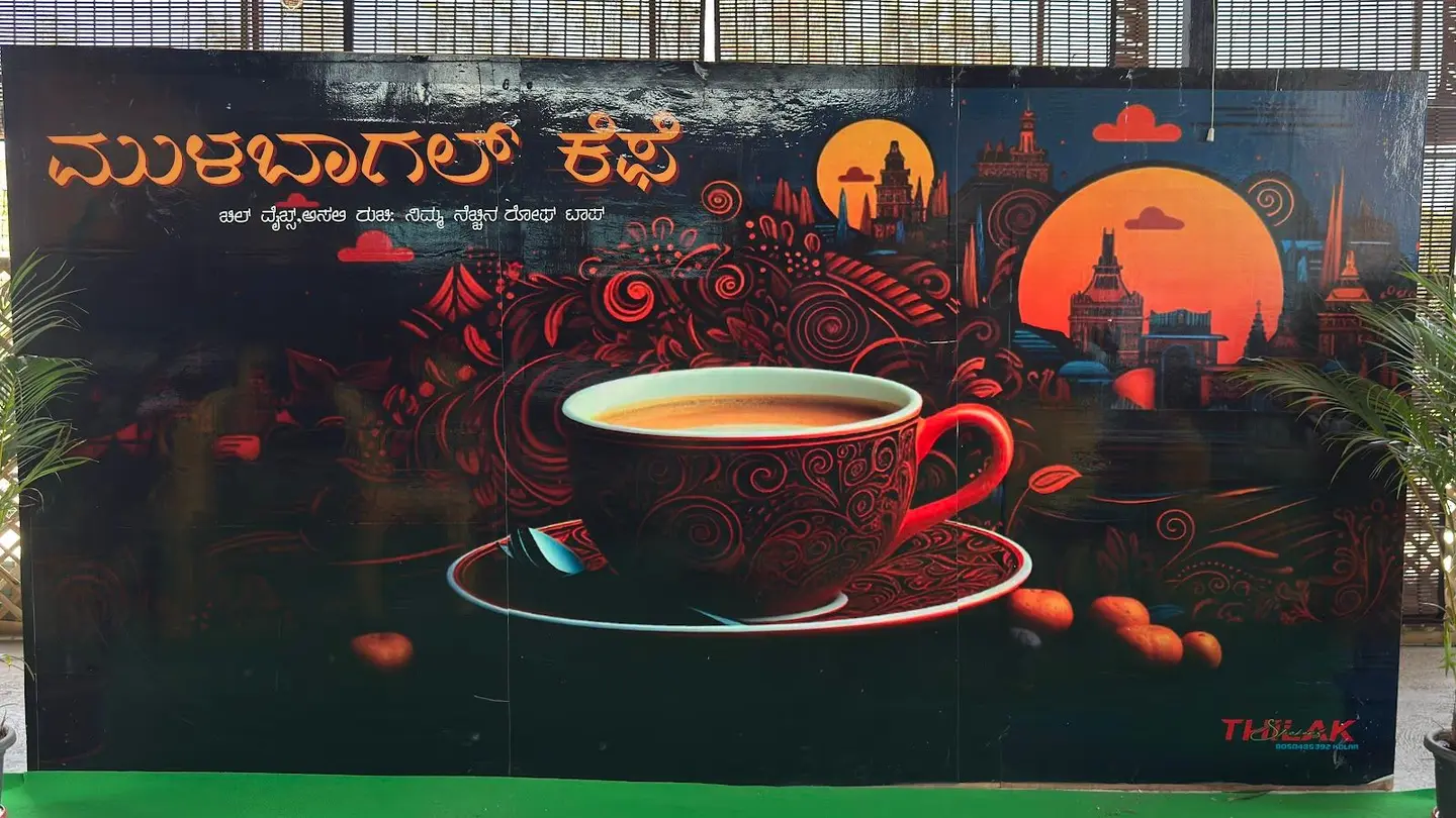 The hand-painted mural: the café's name in Kannada in orange, a red coffee cup, ornamental red scrollwork and temple silhouettes against two orange suns on a black wall.